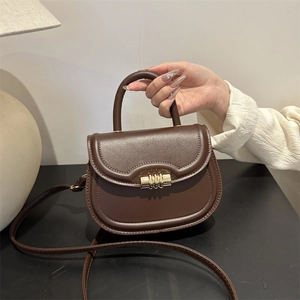 Dark brown leather saddle bag with gold metal lock being held in a stylish indoor setting