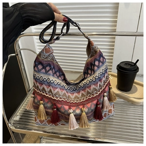 Détail du sac hobo tissé avec motifs géométriques, pompons colorés et bandoulière tressée