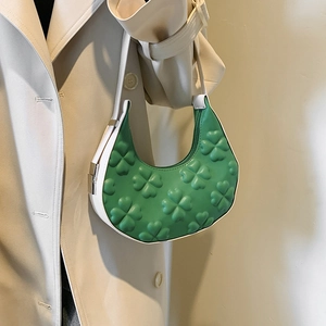Green hobo bag with embossed clover pattern and white strap shown on a model's shoulder