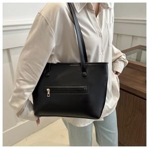 Dettaglio di borsa tote in pelle nera con texture liscia e tasca con zip in metallo dorato