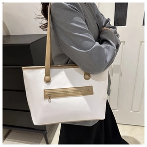 Dettaglio della borsa tote crema minimalista con manici marroni e tasca con zip in metallo