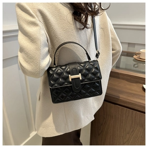 Detail of black quilted leather crossbody bag with golden T-buckle worn on beige blazer