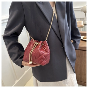 Close-up of quilted dark red bucket bag featuring pearl drawstring and gold chain strap