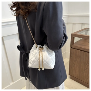 Close-up of a white quilted bucket bag featuring a gold chain and pearl drawstrings