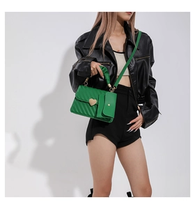 Detail of green quilted handbag with gold heart lock and mini pouch worn by model
