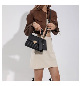 Detail view of black quilted leather handbag with gold heart buckle and pleated top handle