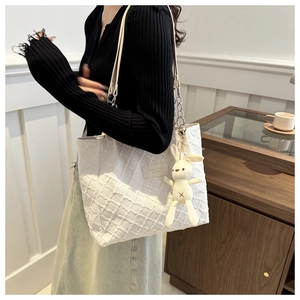 Detail of white tote bag with woven texture, leather chain strap and plush bunny charm