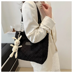 Detail of black textured tote bag with metal chain strap and white rabbit pendant charm