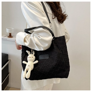 Detail of black quilted tote bag featuring a plush rabbit charm and embossed leather tag