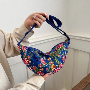 Blaue Halbmond-Umhängetasche mit Blumenmuster und verstellbarem Riemen auf weißem Holzdekor