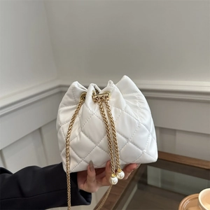 White quilted bucket bag with gold chain strap and pearl drawstring tassels in a soft setting