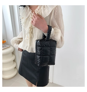 Detail view of a black quilted mini handbag with puffer texture held by a model