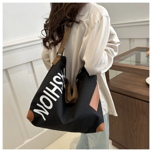 Detail of black canvas tote bag showing large white FASHION print and reinforced corners