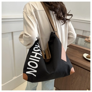 Detail of black canvas tote bag showing white fashion print and brown leather reinforcements
