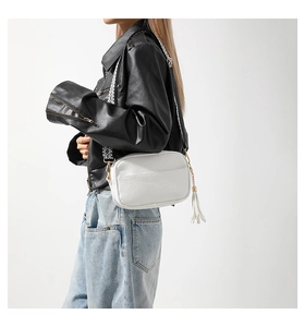 Close-up of white lychee textured crossbody bag with a patterned wide strap and tassel