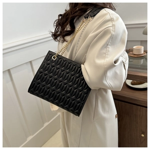 Detail of black quilted shoulder bag with gold chain strap on minimalist beige trench coat