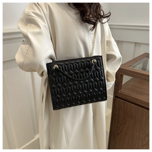 Detail of black quilted shoulder bag featuring gold chain strap and matte texture