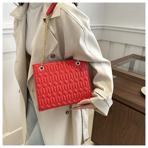 Detail view of red quilted chain bag with gold metal eyelets on beige trench coat