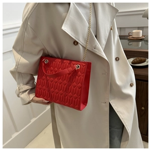 Detail of red quilted tote bag with gold chain strap held by a model in a trench coat