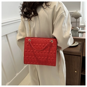 Detail of red quilted faux leather tote bag with gold chain and wide shoulder strap