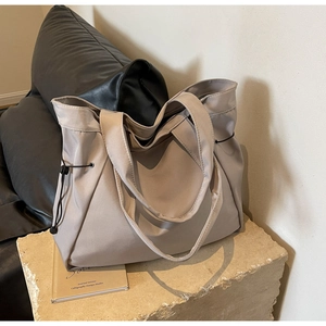 Detail of taupe large-capacity nylon tote bag with drawstring side on a stone surface