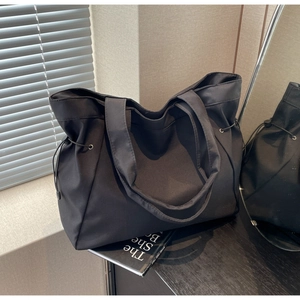 Detail of black nylon tote bag featuring side drawstring cinch and wide shoulder straps