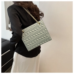 Detail of mint green quilted tote bag with gold chain strap worn by a female model