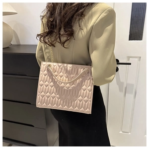 Detail of quilted beige leather tote bag with gold chain strap on model's shoulder