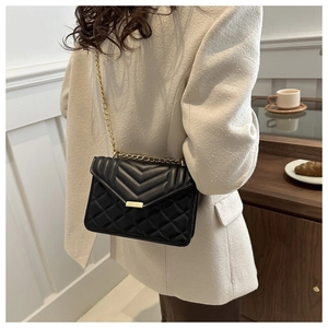 Detail of a black quilted crossbody bag with gold chain strap worn by a model