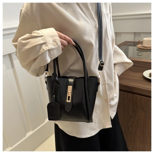 Dettaglio borsa a mano in pelle nera lucida con chiusura dorata e ciondolo alla moda