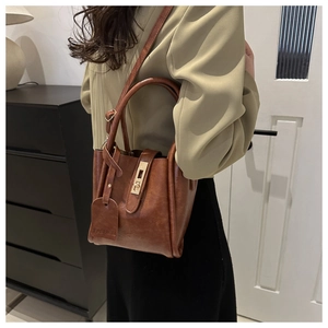 Dettaglio di una borsa a secchiello in pelle marrone con fibbia dorata e cartellino