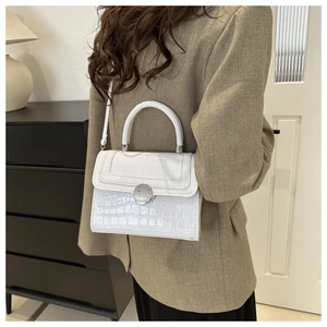 White faux crocodile skin handbag with silver circular clasp worn by a female model