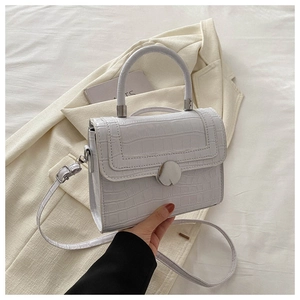 Close-up of white crocodile pattern faux leather handbag with circular metal clasp