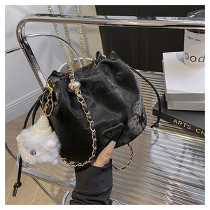 Detail of black drawstring bucket bag with gold chain strap and fluffy monster charm