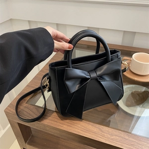 Chic black bucket bag with large bow detail and detachable strap on a wooden side cabinet