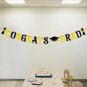 Détail de la bannière Congrats Grad à paillettes noir et or accrochée au mur