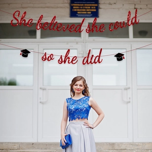 Glittery red 'She Believed She Could So She Did' graduation banner with black cap accents