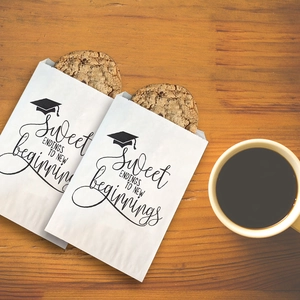 White graduation party favor bag with black Sweet Endings print and cap icon on wood