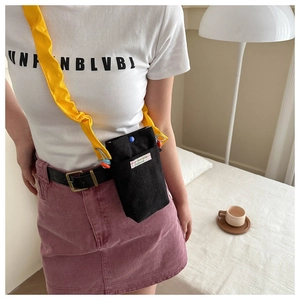 Detail of black corduroy mini crossbody bag with contrasting bright yellow shoulder strap