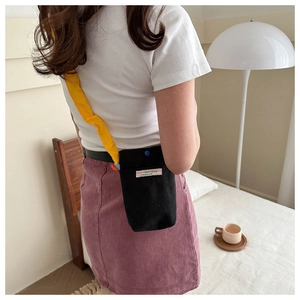 Detail of black corduroy crossbody bag with yellow strap and blue snap button closure