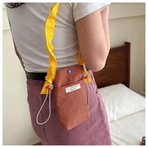 Detail of brown corduroy mini crossbody phone bag with yellow ruffled shoulder strap