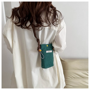 Model wearing dark green corduroy crossbody bag with yellow button and purple drawstring