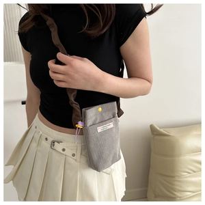 Detail of grey corduroy crossbody bag featuring a yellow button and branded fabric label