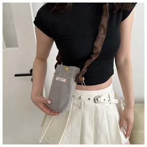 Detail view of gray corduroy mini crossbody bag with pink label and brown pleated strap