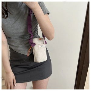 Detail of off-white corduroy mini crossbody bag with purple ruffled strap and orange accents