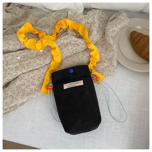 Detail of corduroy crossbody bag with yellow ruffled strap and blue snap closure