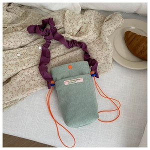 Detail of sage green corduroy phone bag with purple ruffled strap and orange drawstring