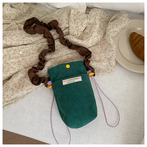 Detail of dark green corduroy crossbody bag with pleated brown strap and logo patch