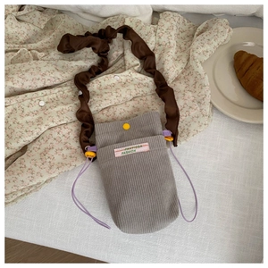 Detail of grey corduroy mini crossbody bag featuring ruffled brown satin shoulder straps