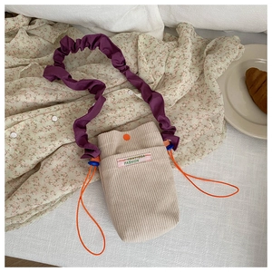 Detail of corduroy crossbody bag with purple ruffled strap and orange button closure